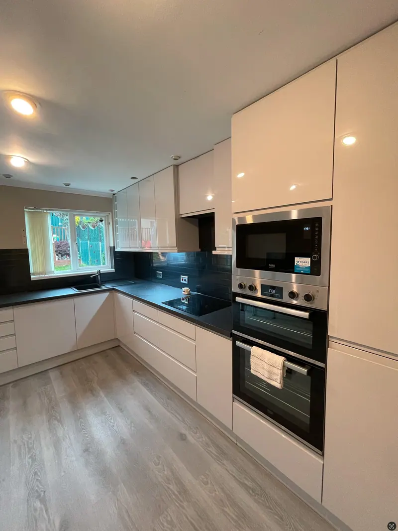 Handleless white gloss kitchen with black worktops and tall oven housing